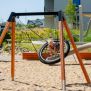 Single Swing (BNS 90cm) ayunan lingkaran dengan rangka kayu dan logam di taman bermain berpasir.